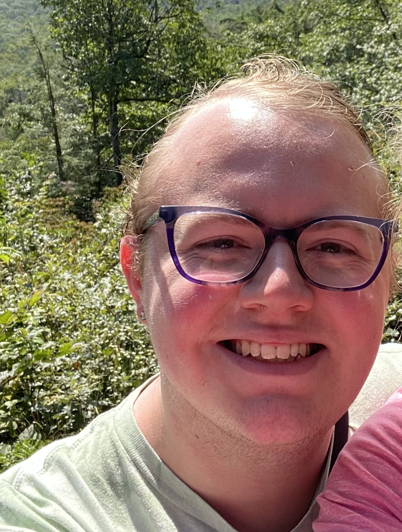 closeup of a smiling person with glasses, outside among foliage